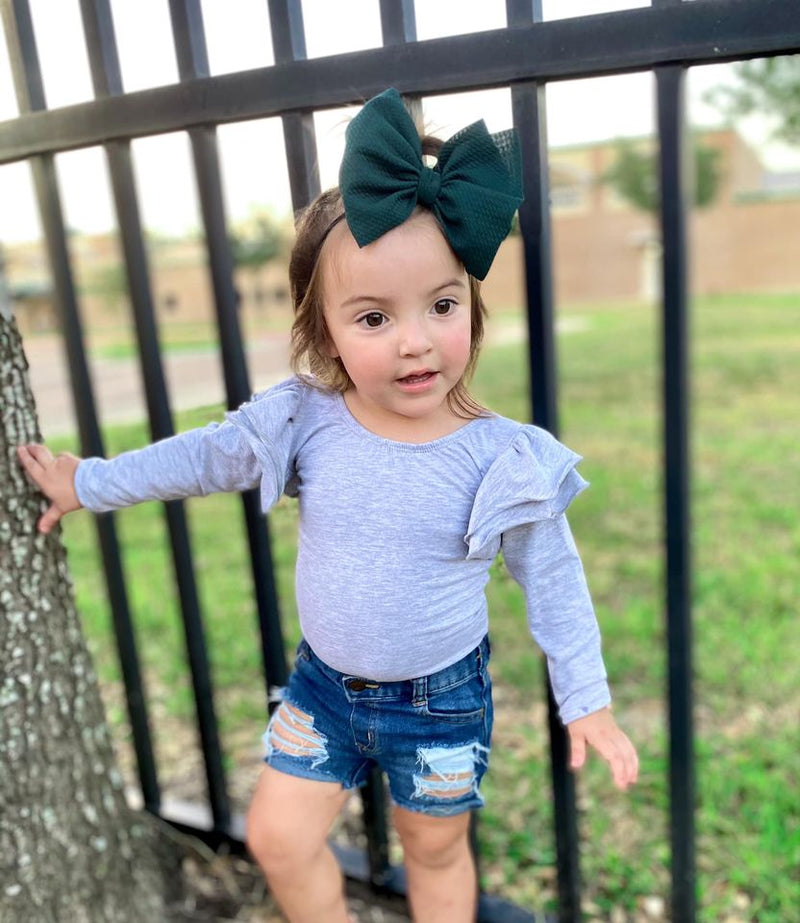 Toddler Girl Outside Wearing Dark Green Bow with Grey Flutter Sleeve Leotard and Jean Shorts 