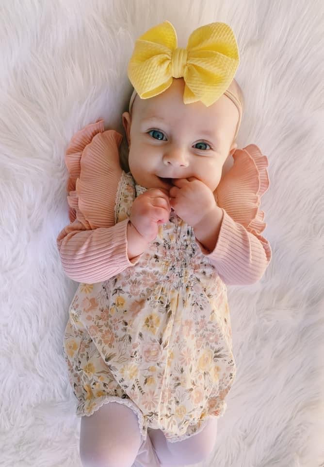 Baby Girl Inside Wearing a Yellow Bow with a Pink Ribbed Flutter Long Sleeve Leotard and a Romper 